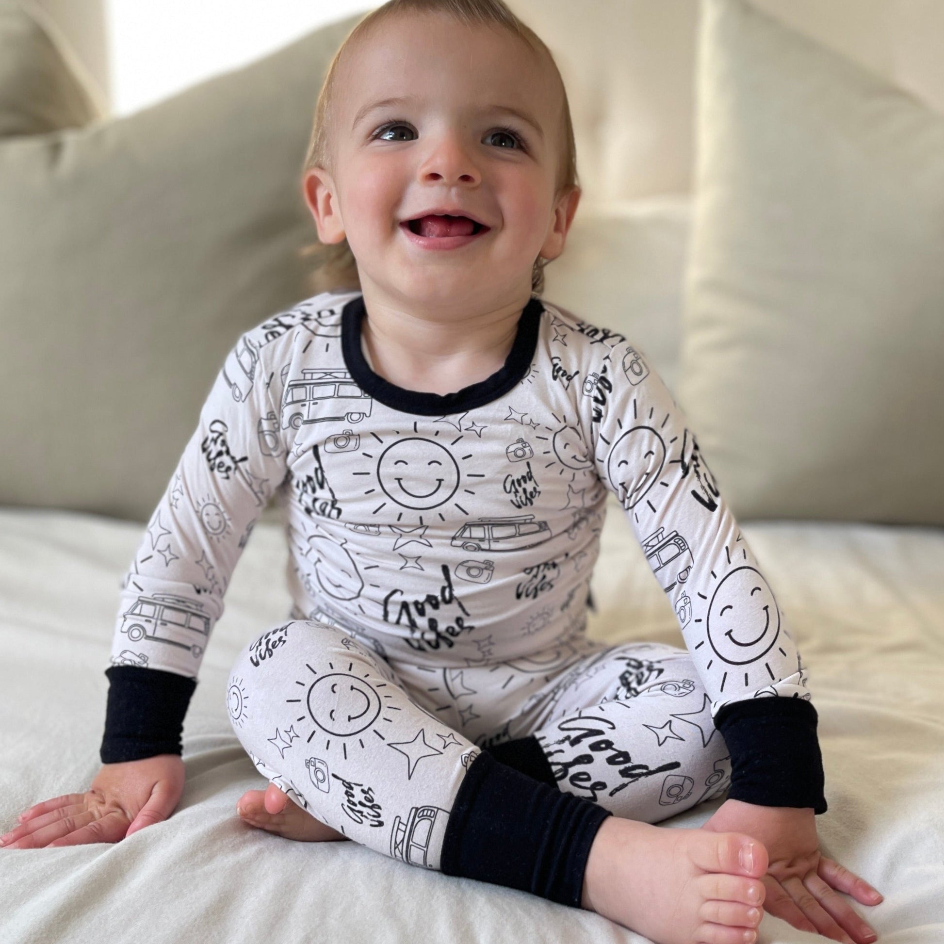 Baby wearing a white onesie with black patterns sitting on a bed.